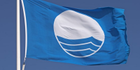 Det Blå Flag i toppen af en flagstand med blå himmel bag