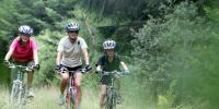 På billedet ses en mor med sin datter og søn på cykeltur gennem skoven