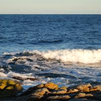 Billedet viser havet, der slå op mod nogle klipper. Der er mange bølger. Solen er ved at gå ned